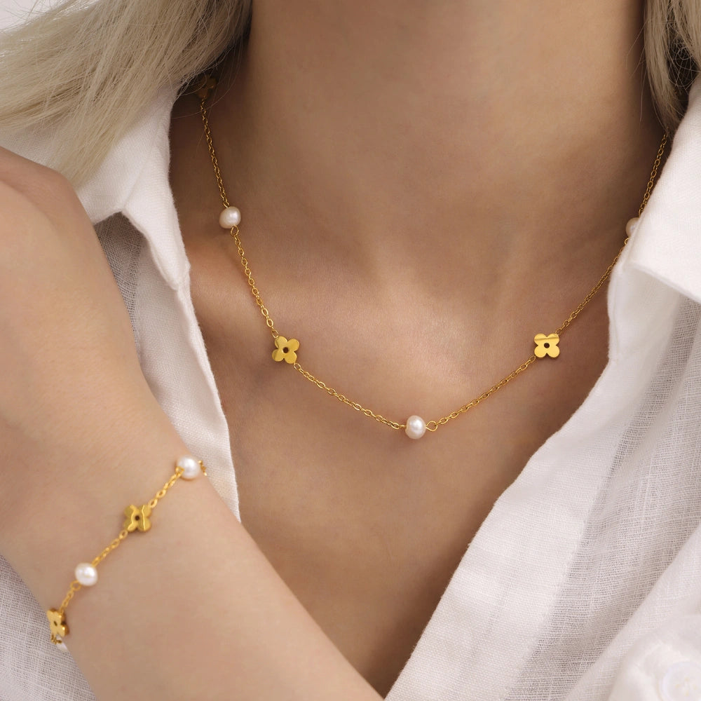 Flat lay of an 18K gold plated stainless steel flower necklace and matching bracelet with freshwater pearls