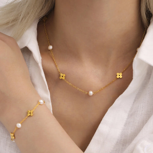 Flat lay of an 18K gold plated stainless steel flower necklace and matching bracelet with freshwater pearls